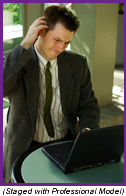 Man sitting at a table in front of a laptop computer scratching his head in confusion (Staged with Professional Model).